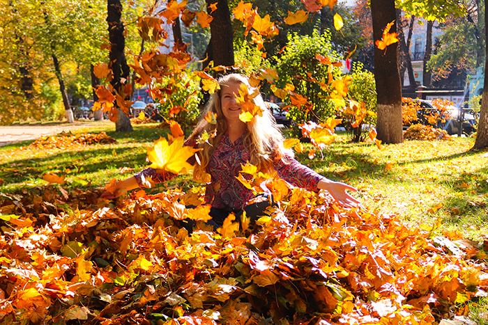 Defocused photo of beautiful young caucasian woman with long blond hair in leaves at the park enjoys autumn. Autumn mood. Lifestyle photo, Selective focus, motion blur.